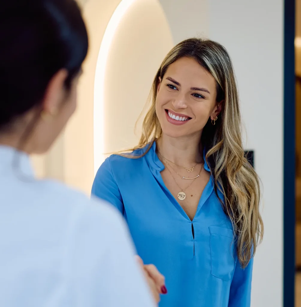 Woman in blue blouse smiling and shaking hands with a doctor in a bright clinic.